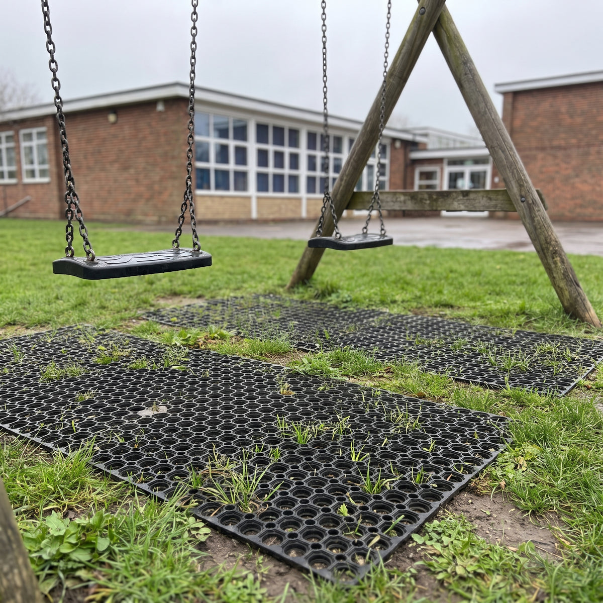 Rubber grass mats laid under a wooden swing set on a school playing field