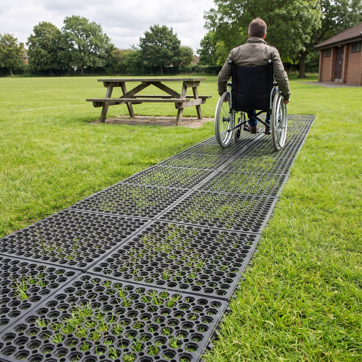 Wheelchair user on an accessible path of interlocking rubber grass mats laid two mats wide across a park lawn, with grass growing through the holes
