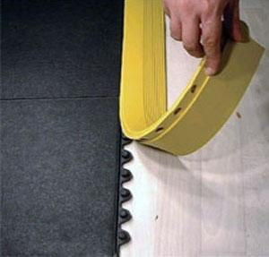 Yellow ramped edge strip being clipped onto the interlocking edge of a black rubber tile