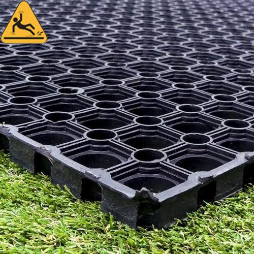 Close-up of the edge of a 23mm rubber grass mat on grass, showing its depth and open-hole lattice